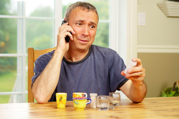 Caucasian man, alone, sit at a table, day, worrying about the pills he is supposed to take.