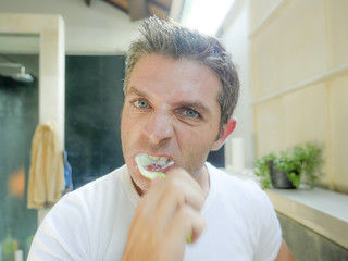 oung attractive white man with blue eyes at home bathroom brushing tooth with toothbrush...