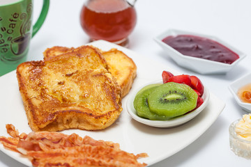 French toast preparation: French toasts cooked and served with fruit, bacon, honey, jam and coffee