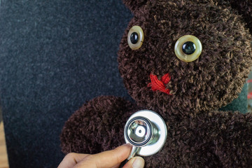 Doctor's hand holding stethoscope put on cute brown handmade fluffy doll with pitty eyes, healthcare for children or kids, medical learning class