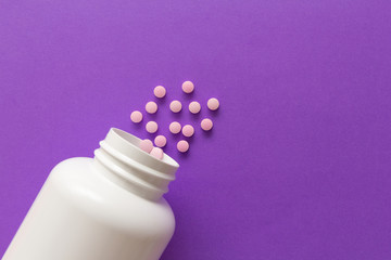 Group pink tablets. Capsules spilling out of white bottle. Violet background.