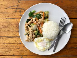 stir-fried chicken with mixed vegetables and fried egg in thai style with rice in white dish on old wooden table. Asian thai food.