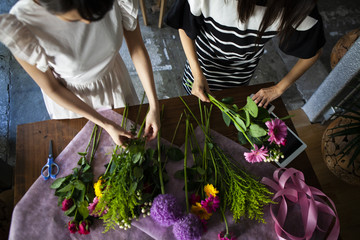 机に広がる色とりどりの花を切り揃え、花束を作る女性二人