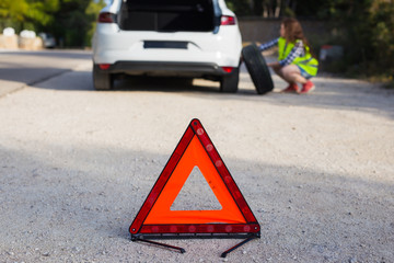 Triangular sign of the accident on the background of a girl about to change the wheel