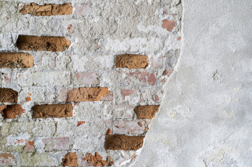 The brick wall is partially cleared from plaster to the basis of red bricks. Background, texture.
