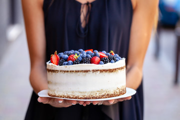 The girl is holding a cake with forest berries, strawberries, blueberries, on the street in the city. A concept for the production of cakes, bakeries, restaurants. Background image