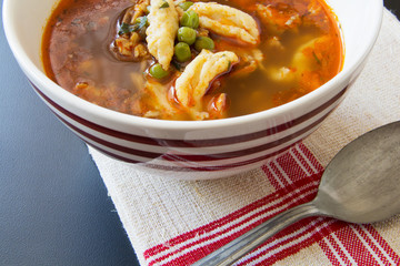 Romanian chicken with dumpling and peas soup in a red and white striped ceramic bowl on an antique vintage hemp homemade towel and antique spoon.