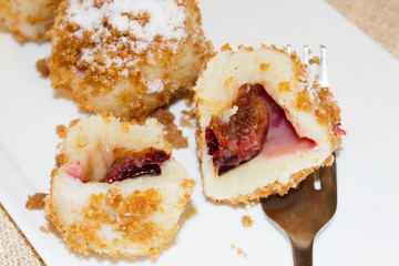 Close up of a plate of sweet plum dumplings with the front dumpling sliced in half. Romanian European traditional sweet dessert.
