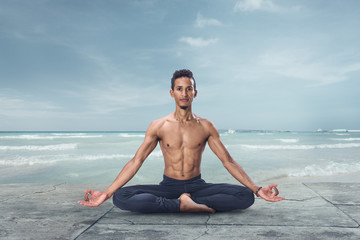 Young man is meditating on the beach