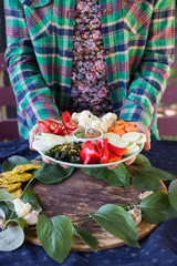Woman hands holds. Vegan Buddha Bowl dish. Raw and cooked vegetables. Carrot, red bell pepper, cauliflower, seaweed, onion, tomato, cucumbers, tomato sauce, sesame seeds. Raw vegan vegetarian food