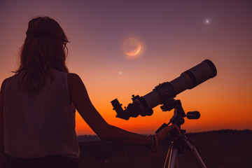 Obraz premium Girl looking at lunar eclipse through a telescope. 