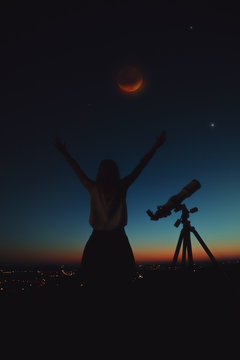 Girl looking at lunar eclipse through a telescope. 