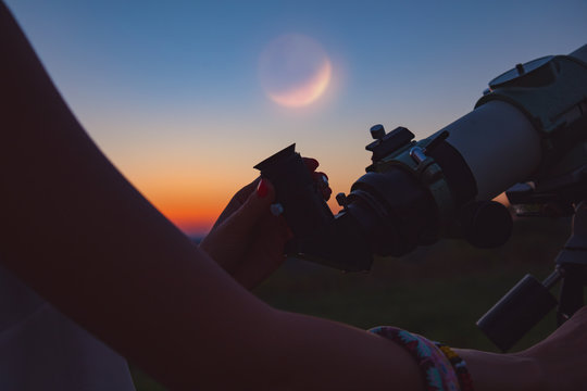 Girl looking at lunar eclipse through a telescope. 