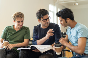 Confident Hispanic guy explaining task to Indian student during break. Serious mentor working with...