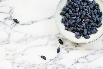 Fresh ripe honeysuckle berries in a ceramic bowl on a grey marble table