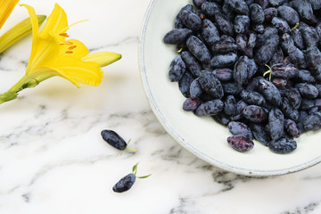 Fresh ripe honeysuckle berries in a ceramic bowl on a grey marble table