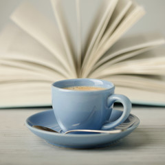Coffee in a light blue cup and book in blue cover on a wooden background.