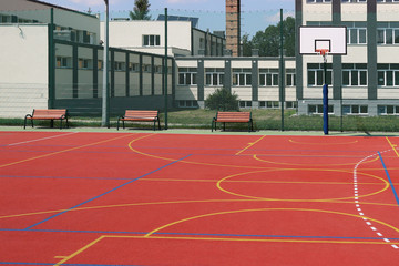 Obraz premium Lubno, Poland - july 9 2018:Basketball shield in an open stadium in the courtyard of a rural school. Sports ground for football with artificial multicolored coating. Lighting on natural sources 