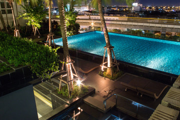 Pool at night with lush greenery and lighting for home design and landscaping in the backyard.  Night shadows and reflections on the pool water.