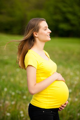 pregnant woman in yellow t shirt on a green meadow in spring