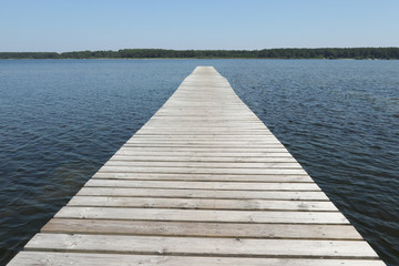 wooden pier flows into the blue water of the lake in summer