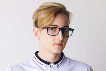Boy teenager in glasses and white shirt poses in white studio, close up