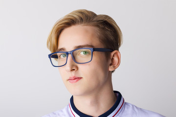 Handsome boy teenager in glasses and white shirt poses in white studio, close up