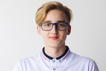 Handsome boy teenager in glasses and white shirt poses in white studio