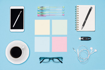 Office desk flat lay. Top view of working space table with morning coffee, smartphone and stationery, office supplies on pastel blue colored background. Back to school concept.