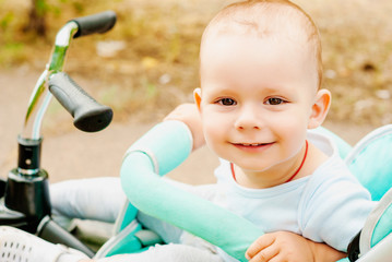 Little baby boy sitting in the stroller at the green garden.