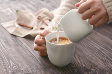 Woman pouring milk into cup of tea on table