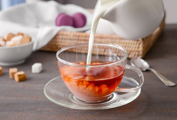 Pouring of milk into cup of tea on wooden table
