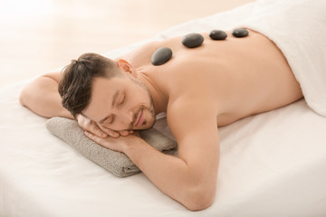 Handsome man having stone massage in spa salon