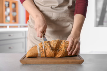 Woman cutting tasty bread on wooden board