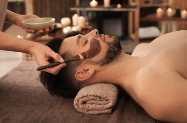 Beautician applying cosmetic mask on man's face in spa salon