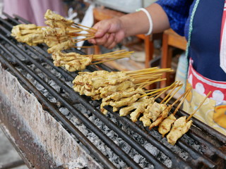 Pork barbeque (Moo Satay) being roasted on a charcoal grill getting ready to be served with peanut sauce - delicious and healthy street food in Thailand