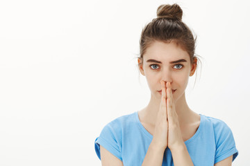 Close-up shot of worried intense cute female student with bun hairstyle, holding hands in pray over face and staring nervously at camera, feeling anxious while waiting for something important happen