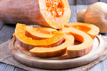 Raw pumpkin sliced into on wooden cutting board on wooden table