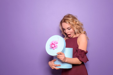 Surprised young woman opening gift box on color background