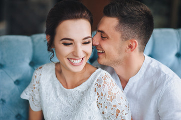 Beautiful newlyweds sitting on a blue sofa in the studio and smiling. A merry groom and a sweet bride laugh. Wedding portrait.
