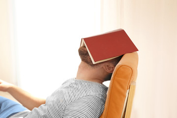 Obraz premium Young man sleeping with book on his face at home