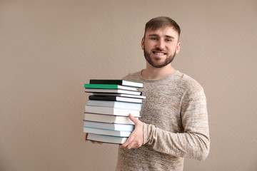 Young man with stack of books on color background