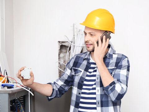 Electrician Talking On Phone Near Distribution Board Indoors