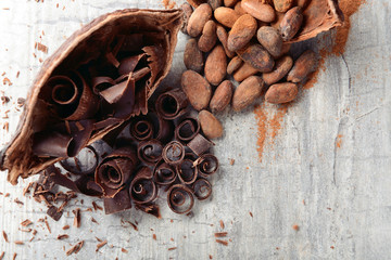 Delicious chocolate curls with cocoa beans on table