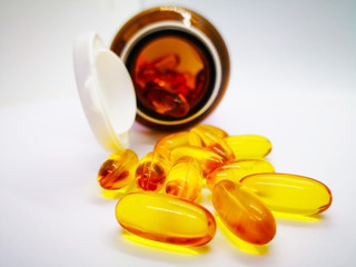 Many oval yellow capsules of fish oil, fatty acids are not made by the body and must be consumed in the diet. There were poured out of glass bottle. Isolated on white background, selective focus.