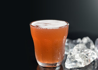 Cold drink with iced cube on black background.