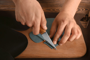 Fototapeta na wymiar Man cutting leather on wooden board in workshop