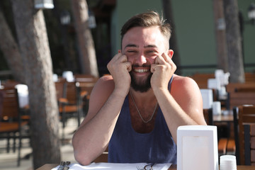 Young man with black hair and beard sitting in a restaurant in the Park in a summer evening