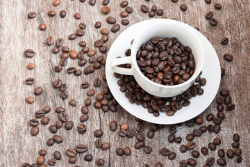 Coffee beans in white cup on wooden table with copy space.