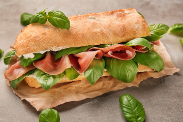 Tasty sandwich with prosciutto and basil on table